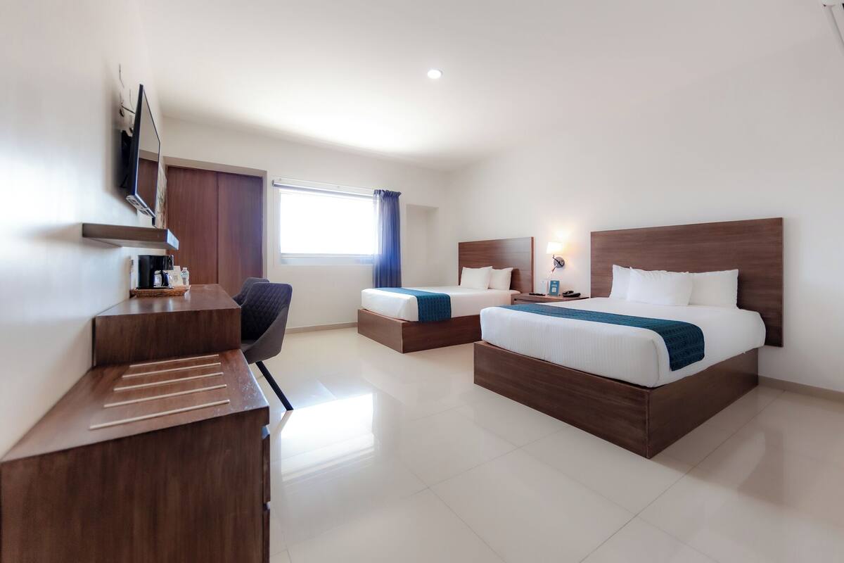 Una habitación de hotel con dos camas, un escritorio, un televisor y una ventana con cortinas.