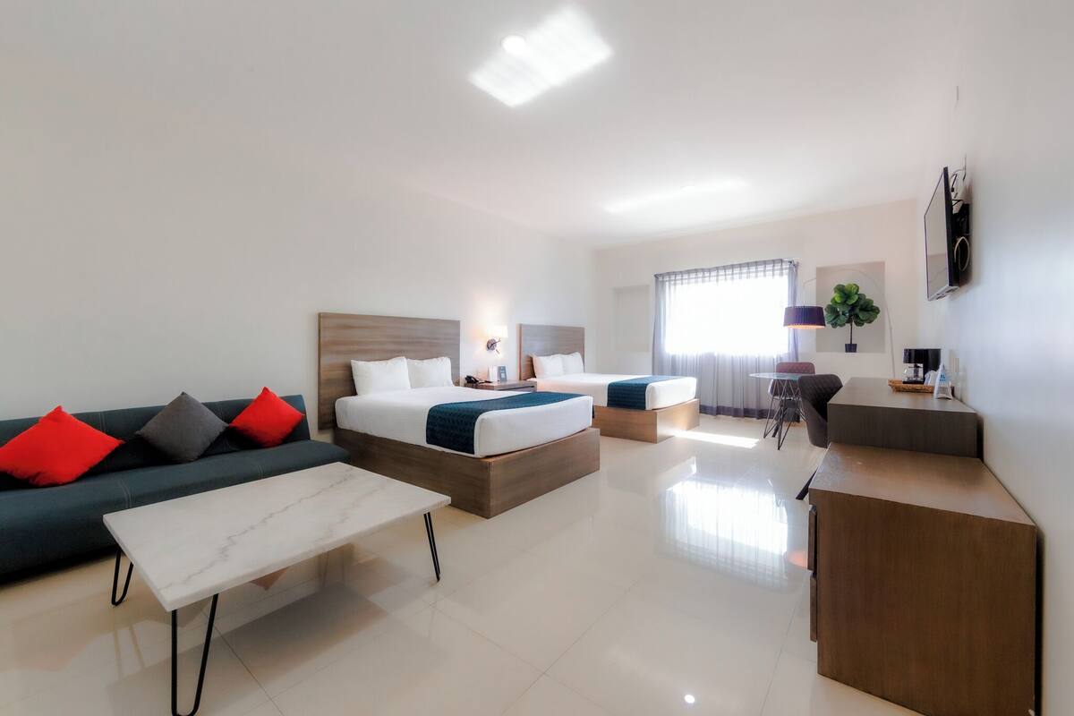 Una habitación de hotel moderna con sofá, dos camas, un escritorio y una mesa de comedor.