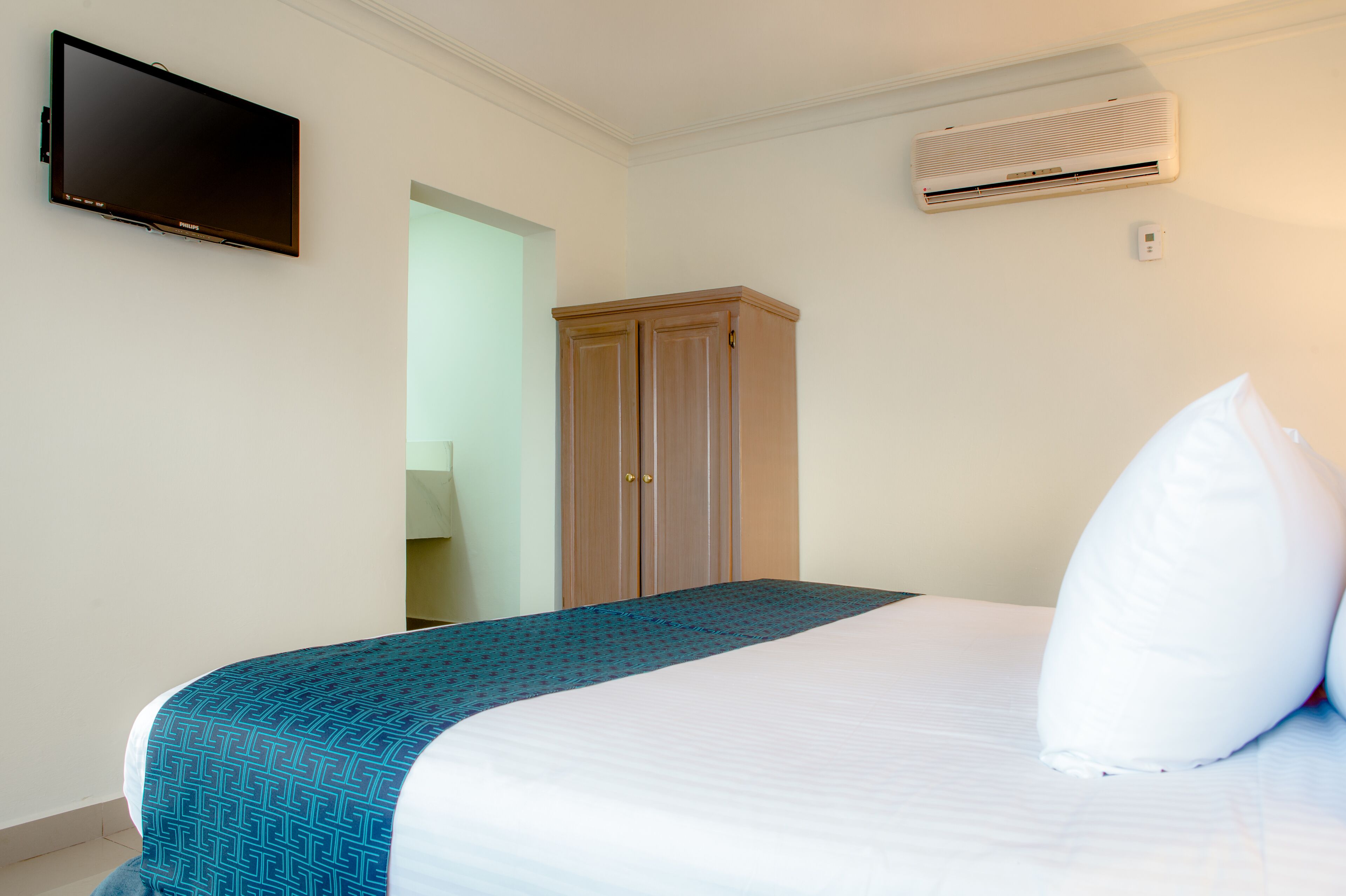 Une chambre d’hôtel équipée d’un lit, d’un téléviseur fixé au mur, d’un appareil de climatisation et d’une armoire.