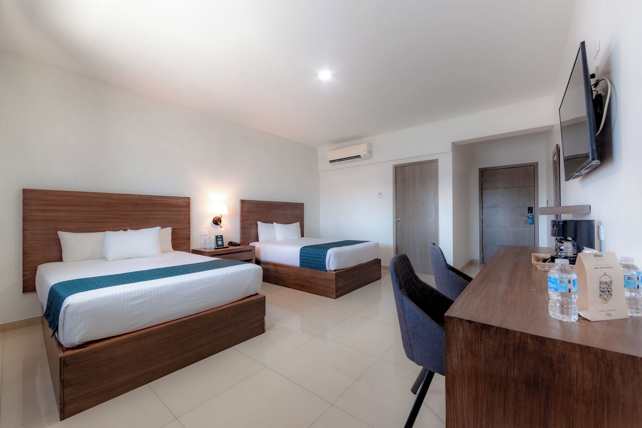 Una habitación de hotel con dos camas, un escritorio con una silla, un televisor y una cafetera.