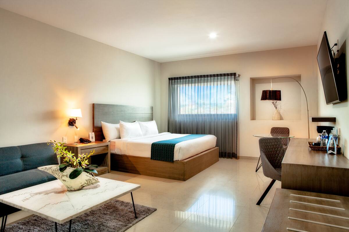 Una habitación de hotel con cama, sofá, escritorio, lámpara y televisión.
