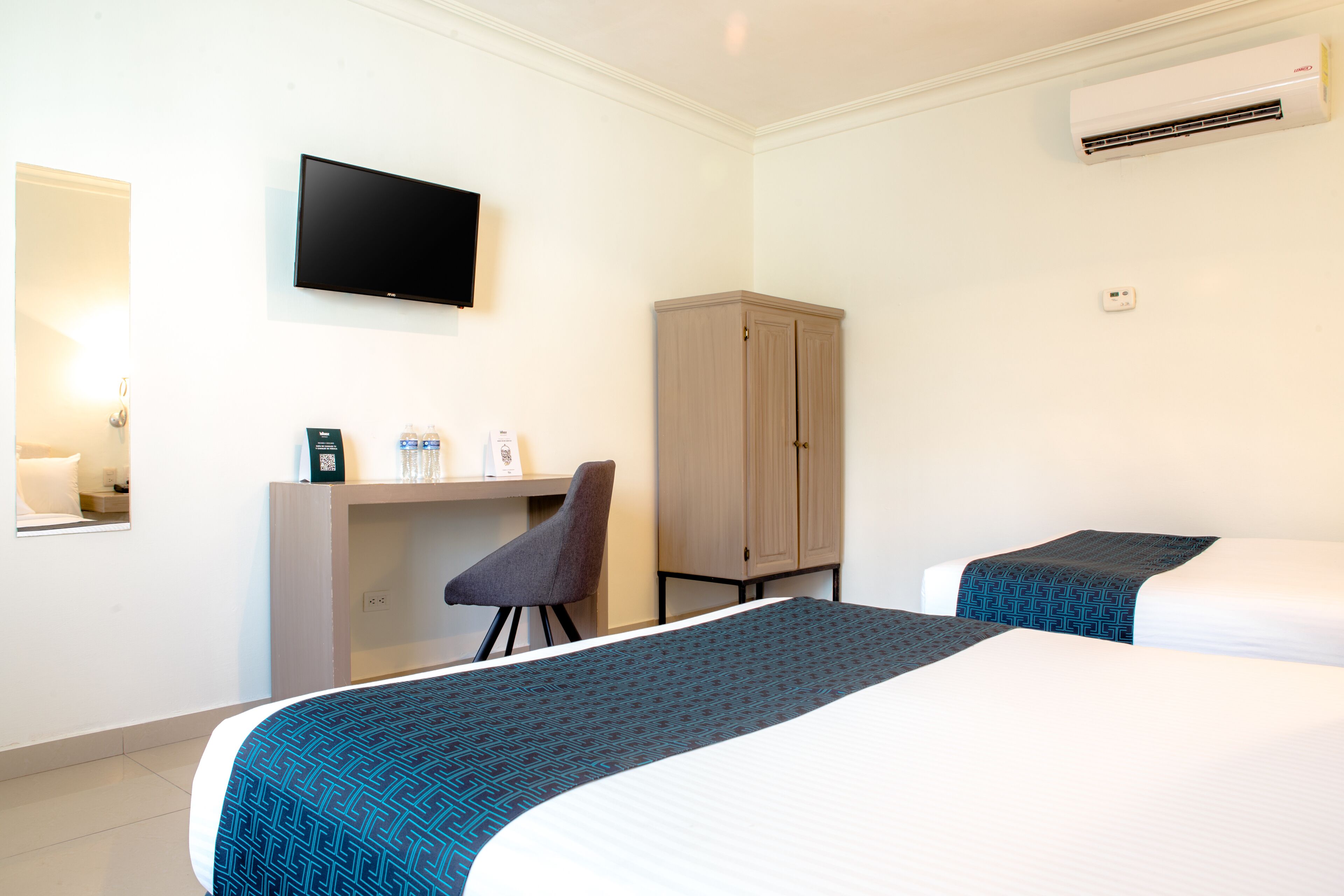 Habitación de hotel con cama, escritorio, silla, armario, televisión y aire acondicionado.