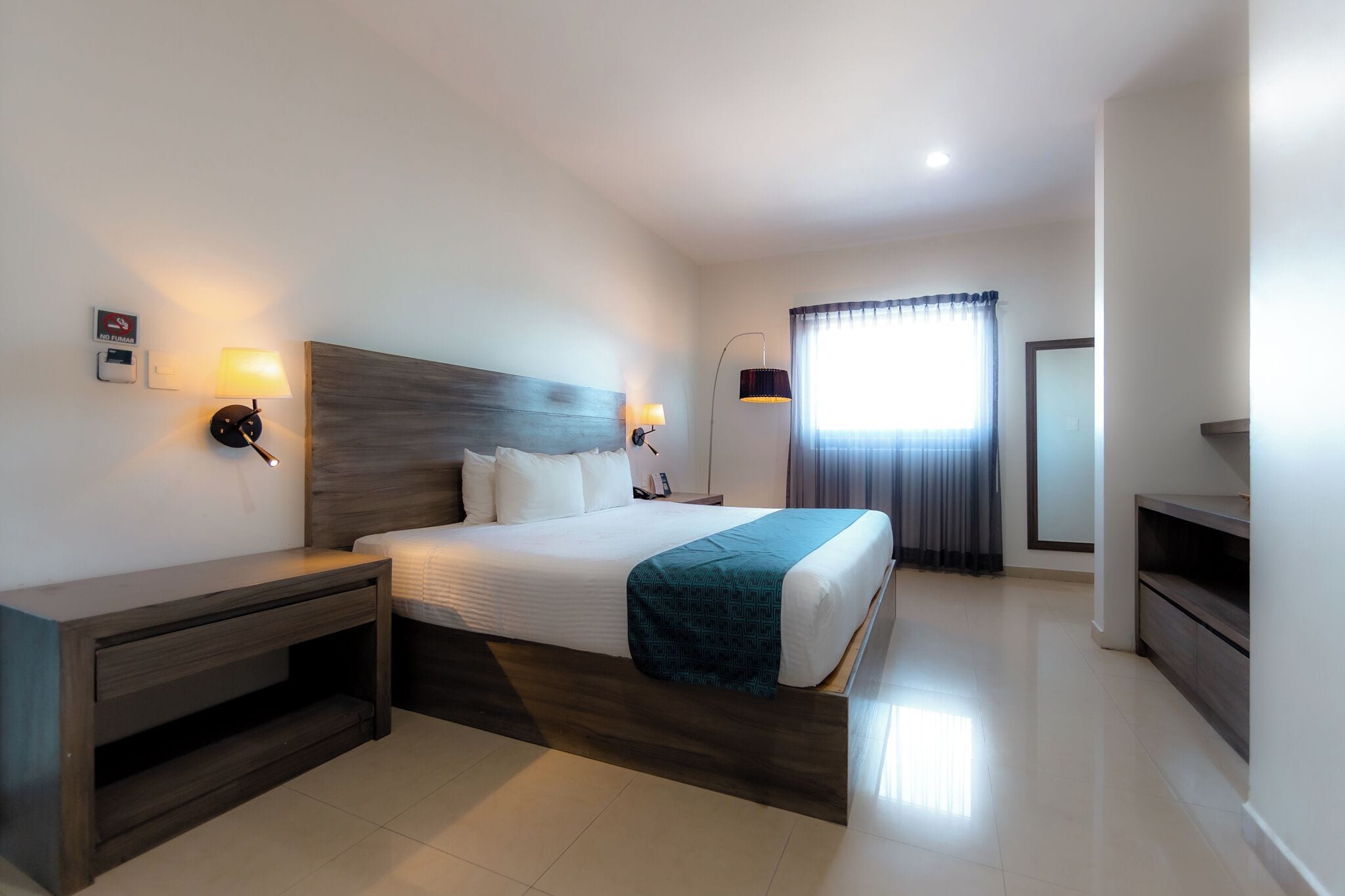 Quarto de hotel moderno com uma cama grande, mesas de cabeceira, escrivaninha e televisão.