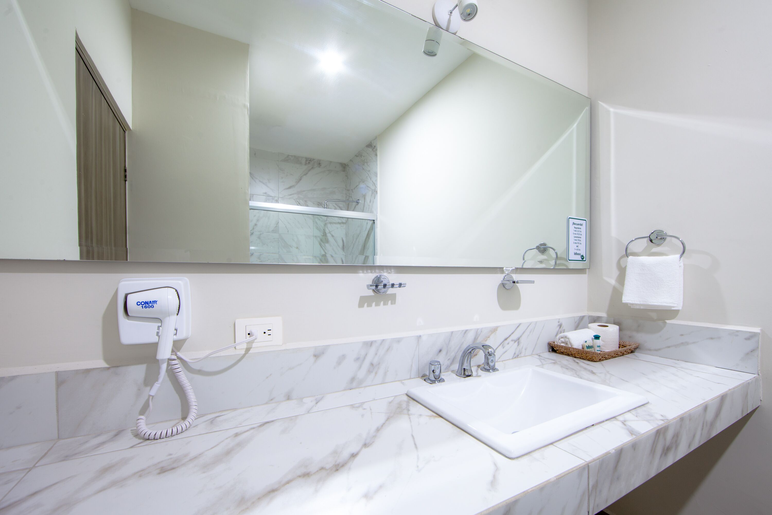 Un baño moderno con encimera de mármol, un espejo grande, ducha y un secador de pelo conectado.