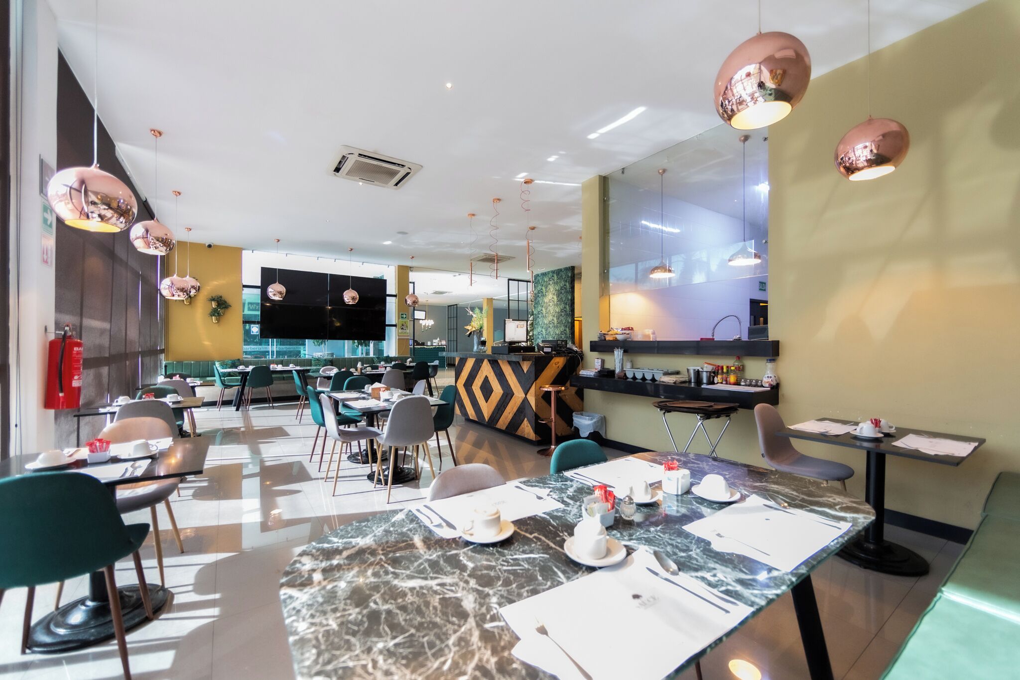 Un restaurante moderno con mesas de mármol, sillas verdes y lámparas colgantes rosadas.