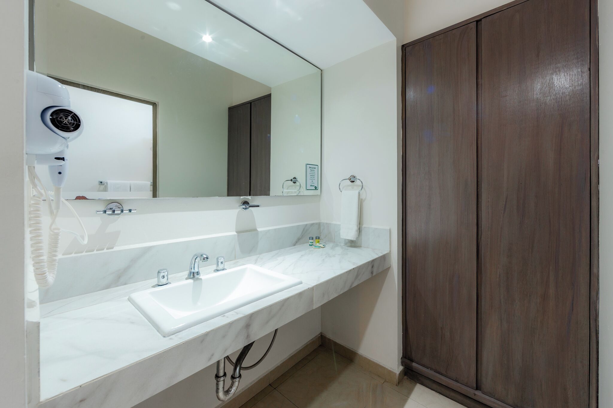 Un baño con lavamanos de mármol blanco, un secador de pelo y un armario de madera oscura.