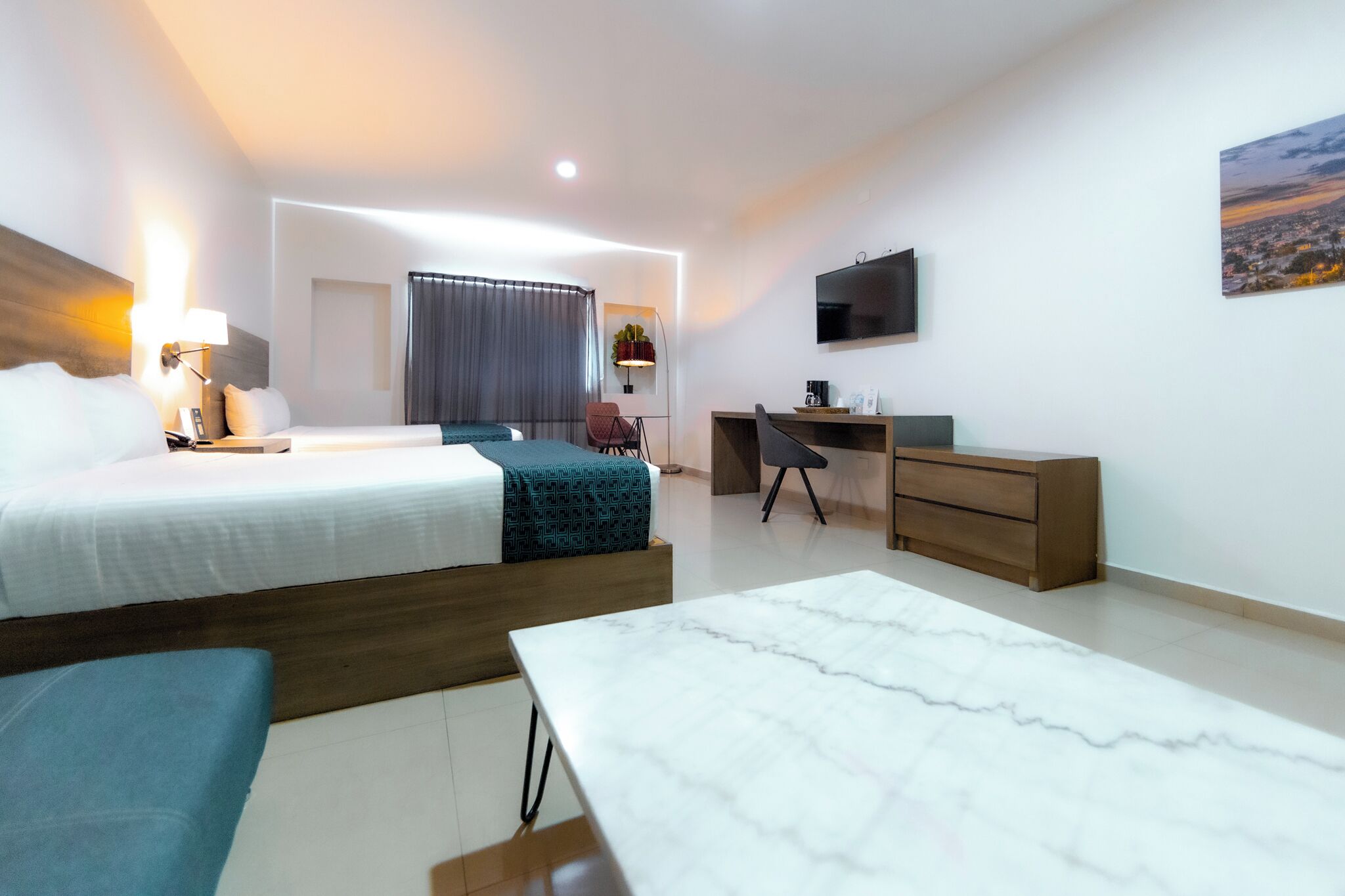 Una habitación de hotel moderna con cama, escritorio, silla y televisor en la pared.