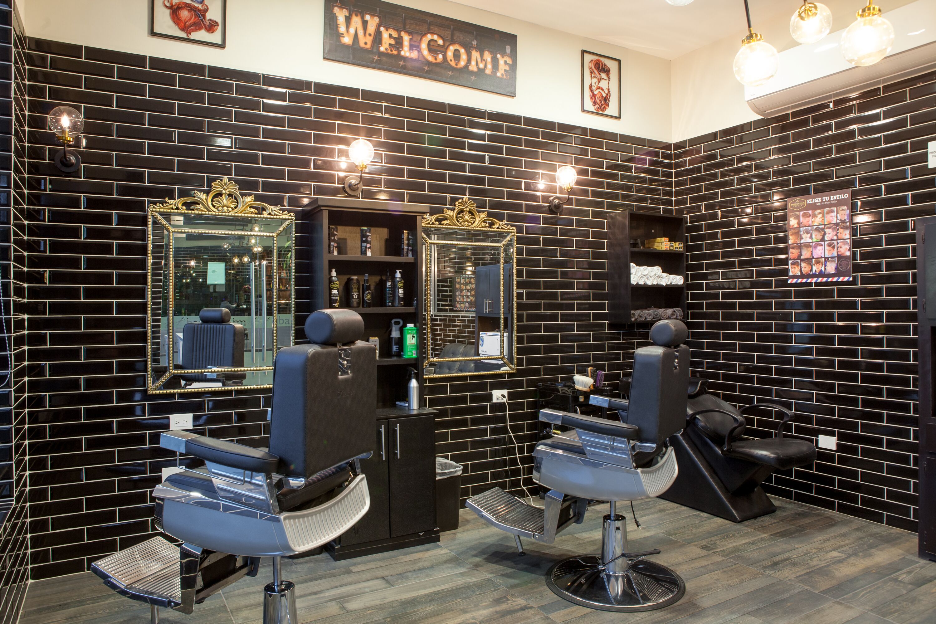 Una barbería moderna con paredes de baldosas negras y dos sillones de barbero.