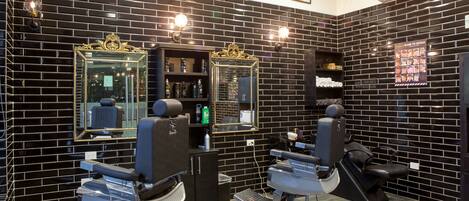 Una barbería moderna con paredes de baldosas negras y dos sillones de barbero.