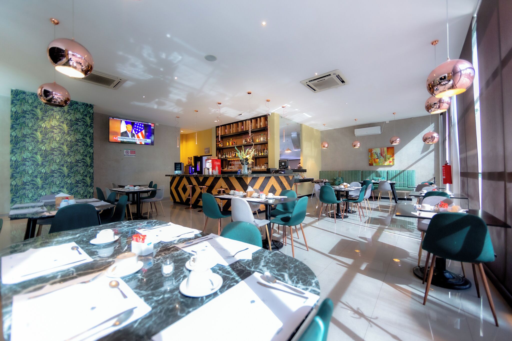 A modern restaurant with marble tables, teal chairs, and a bar area with shelves of bottles.
