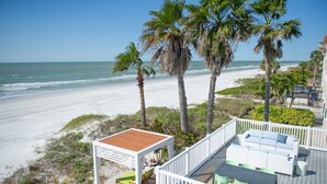 A beachside deck with a white railing, a white sofa, and a table with chairs. - Sunburst Inn (Indian Shores)