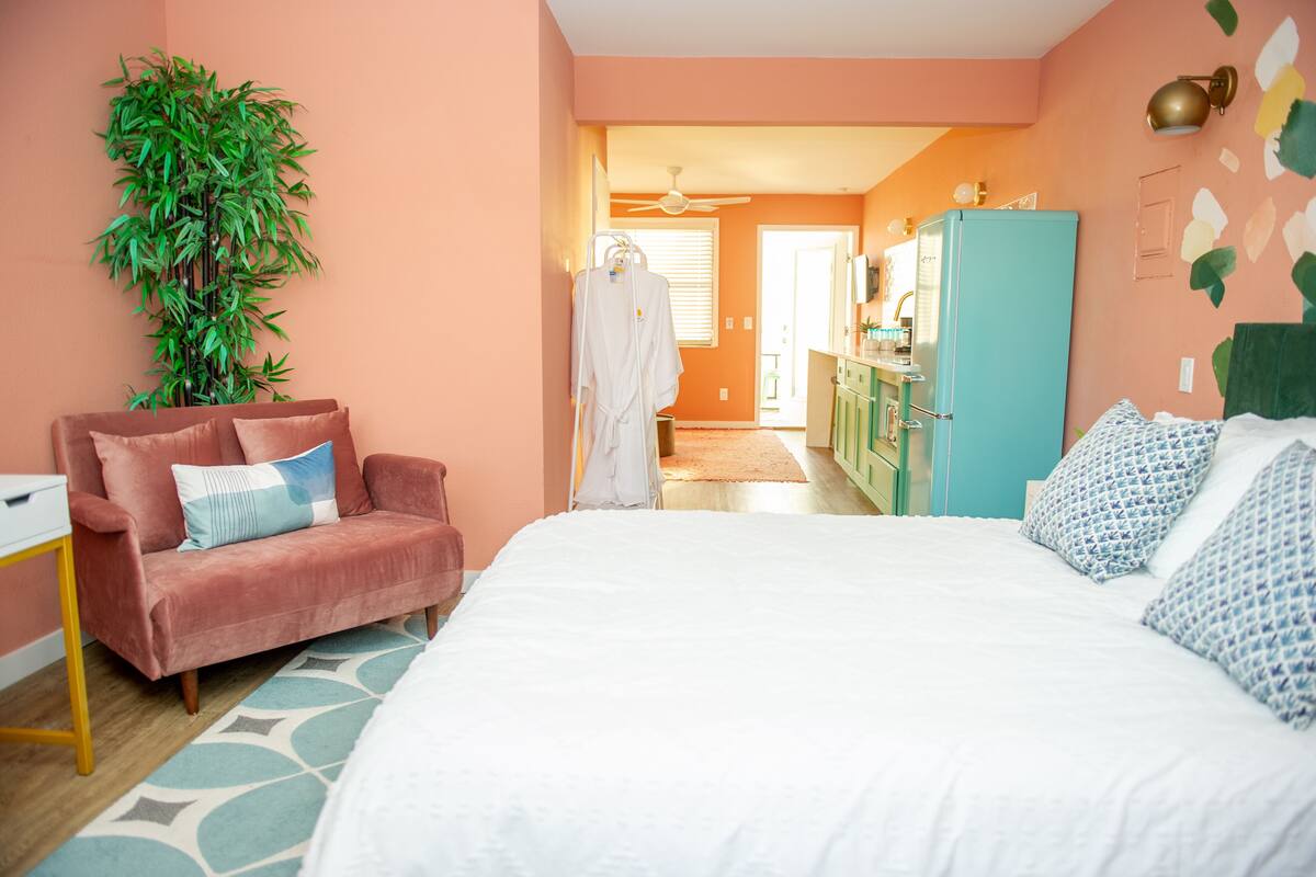 A bedroom with a bed, a pink sofa, a green cabinet, and a large plant.
