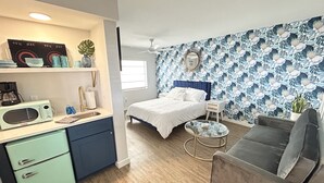 A compact room with a bed, a sofa, a small round table, a kitchenette with a fridge, and a wall with a floral pattern. - Sunburst Inn (Indian Shores)