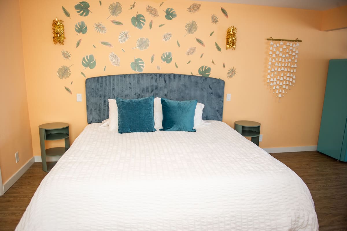A bedroom with a large bed, two nightstands, a teal wardrobe, and a wall with leaf patterns.