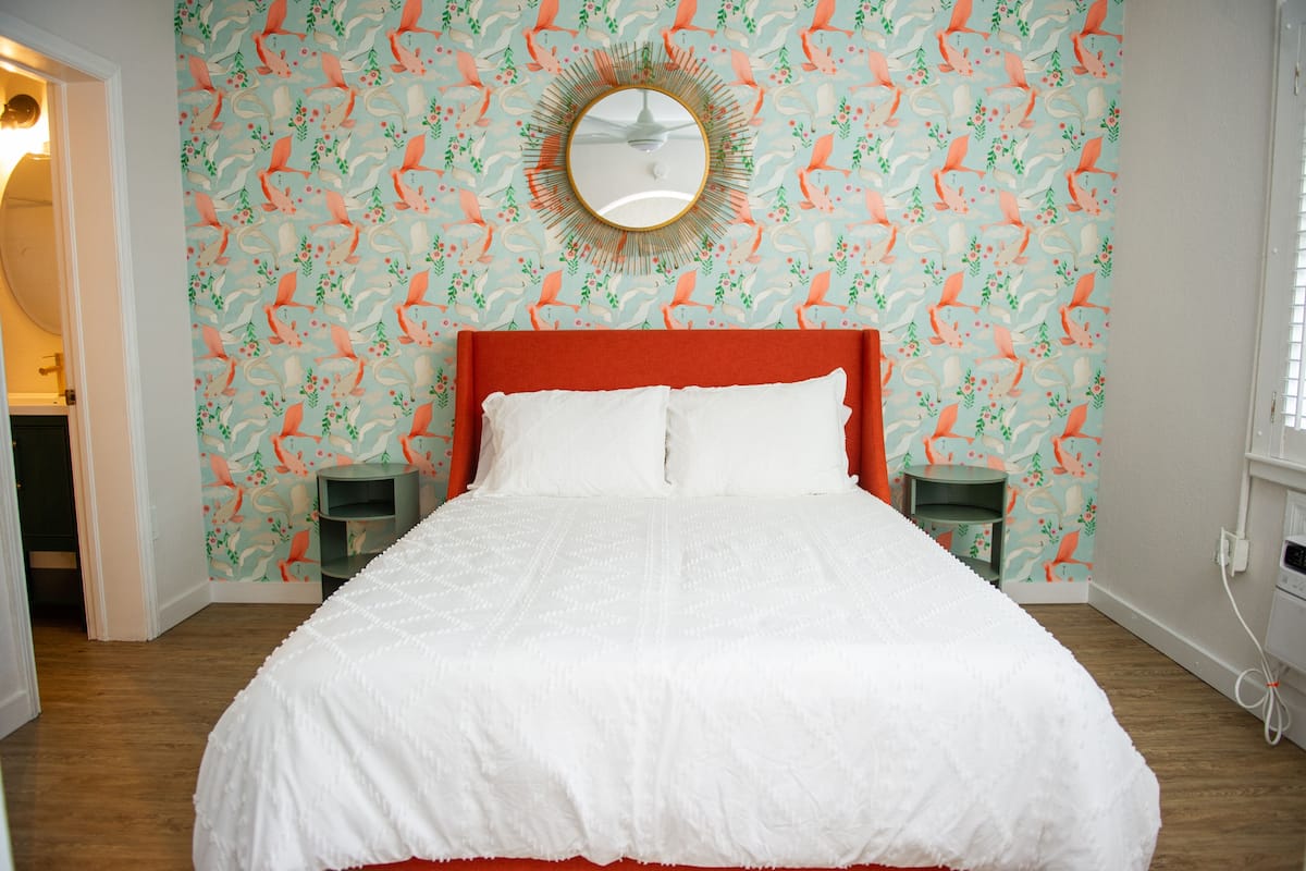 A bedroom with a large bed, a round mirror above it, and a floral wallpaper pattern.