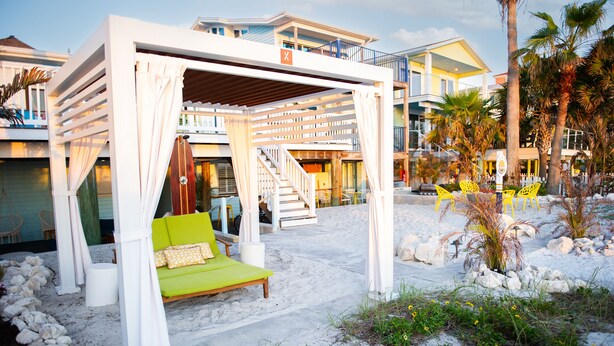 A beachside bed with a green cushion, white curtains, and a wooden bench. - Sunburst Inn (Indian Shores)