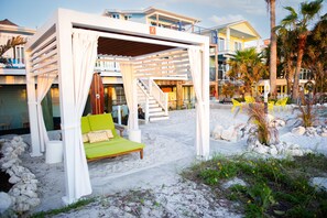 A beachside bed with a green cushion, white curtains, and a wooden bench. - Sunburst Inn (Indian Shores)