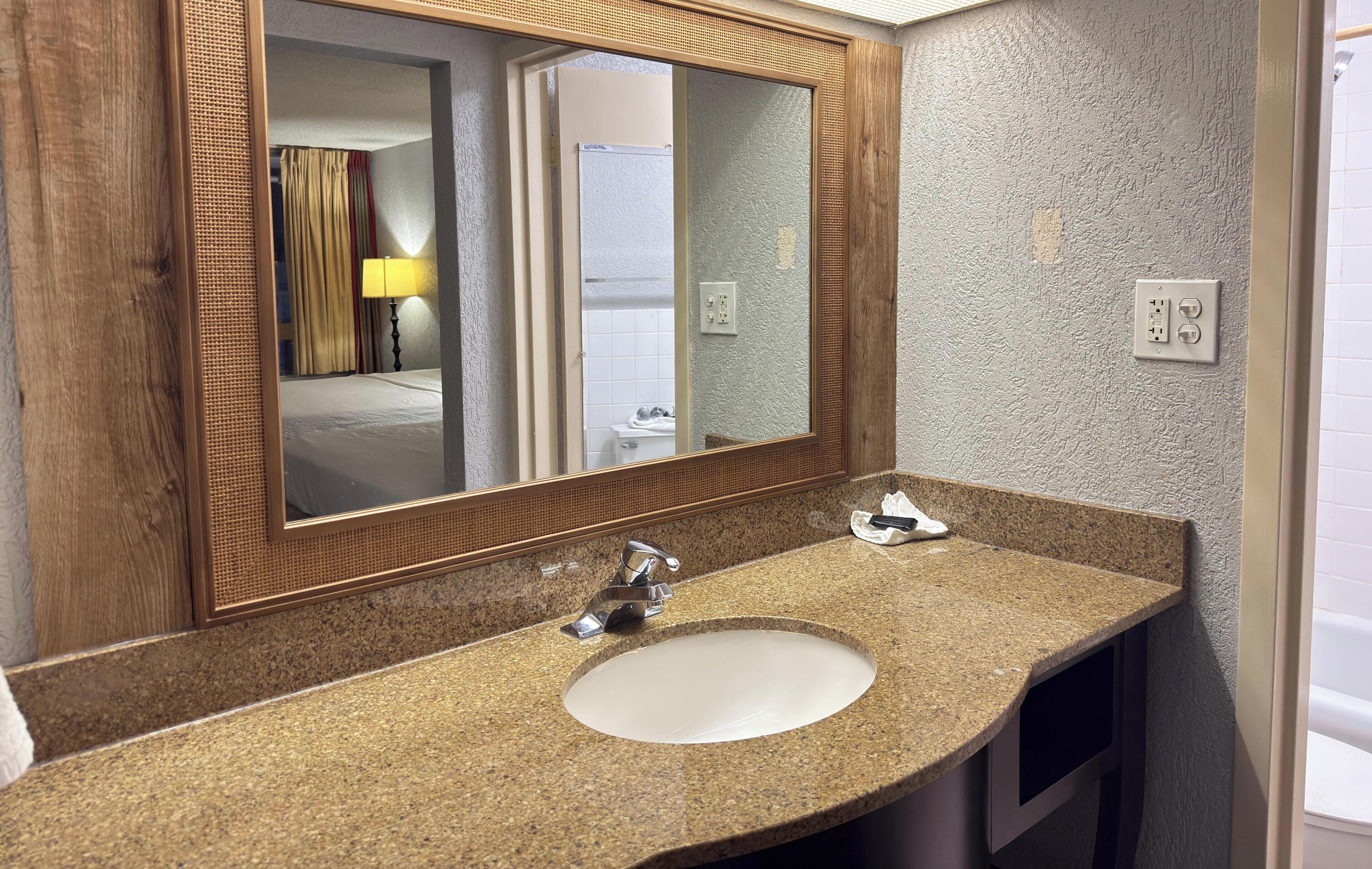 A bathroom with a granite countertop, a white sink, a mirror with a wooden frame, and a visible shower area.