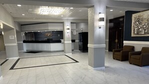 A spacious lobby with a reception desk, a refrigerator, and two armchairs. - The Lodge Hotel and Banquets (Bridgeton)