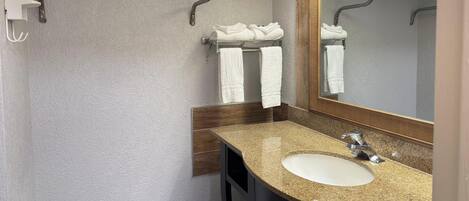 A bathroom with a granite countertop sink, a large mirror, and two towel racks.