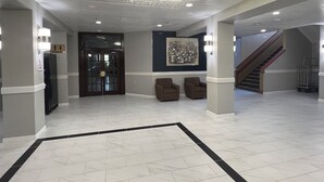 A spacious lobby with a modern ceiling design, a staircase, and a restroom sign. - The Lodge Hotel and Banquets (Bridgeton)