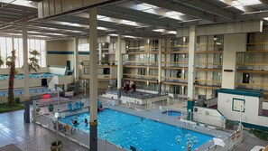 A multi-level indoor swimming pool with a central pool area surrounded by balconies and a covered walkway.