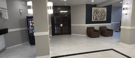 A lobby with a vending machine, two armchairs, a door, and a wall-mounted artwork.