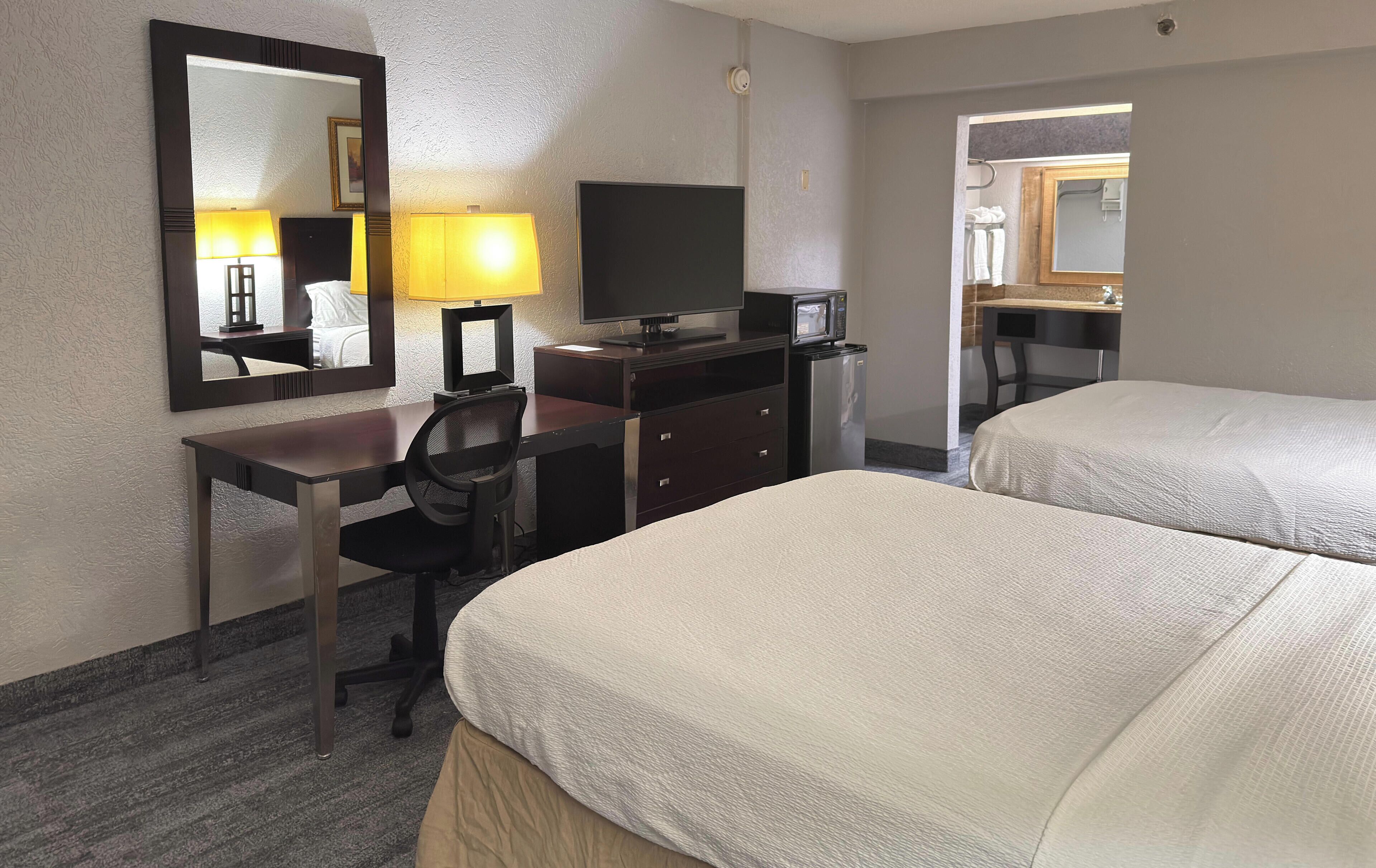 A hotel room with two beds, a desk with a chair, a television, a microwave, and a mirror.