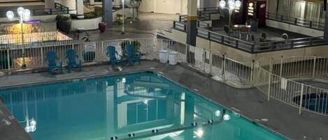 En indendørs swimmingpool med flere balkonplaner, en central trappe og et siddeområde med stole.