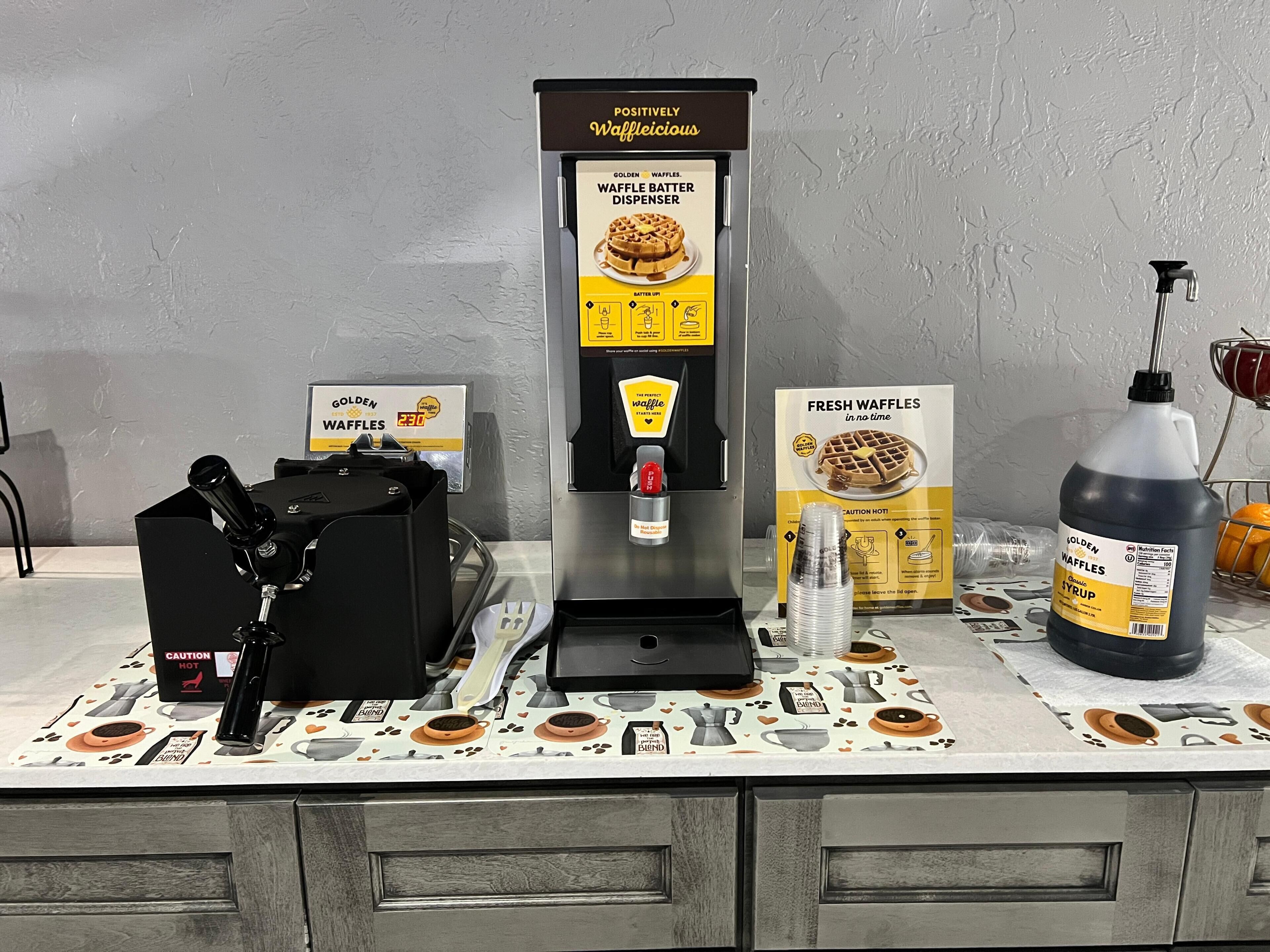 A waffle station with a waffle batter dispenser, a syrup bottle, and a waffle box.