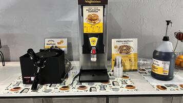 A waffle station with a waffle batter dispenser, a syrup bottle, and a waffle box.