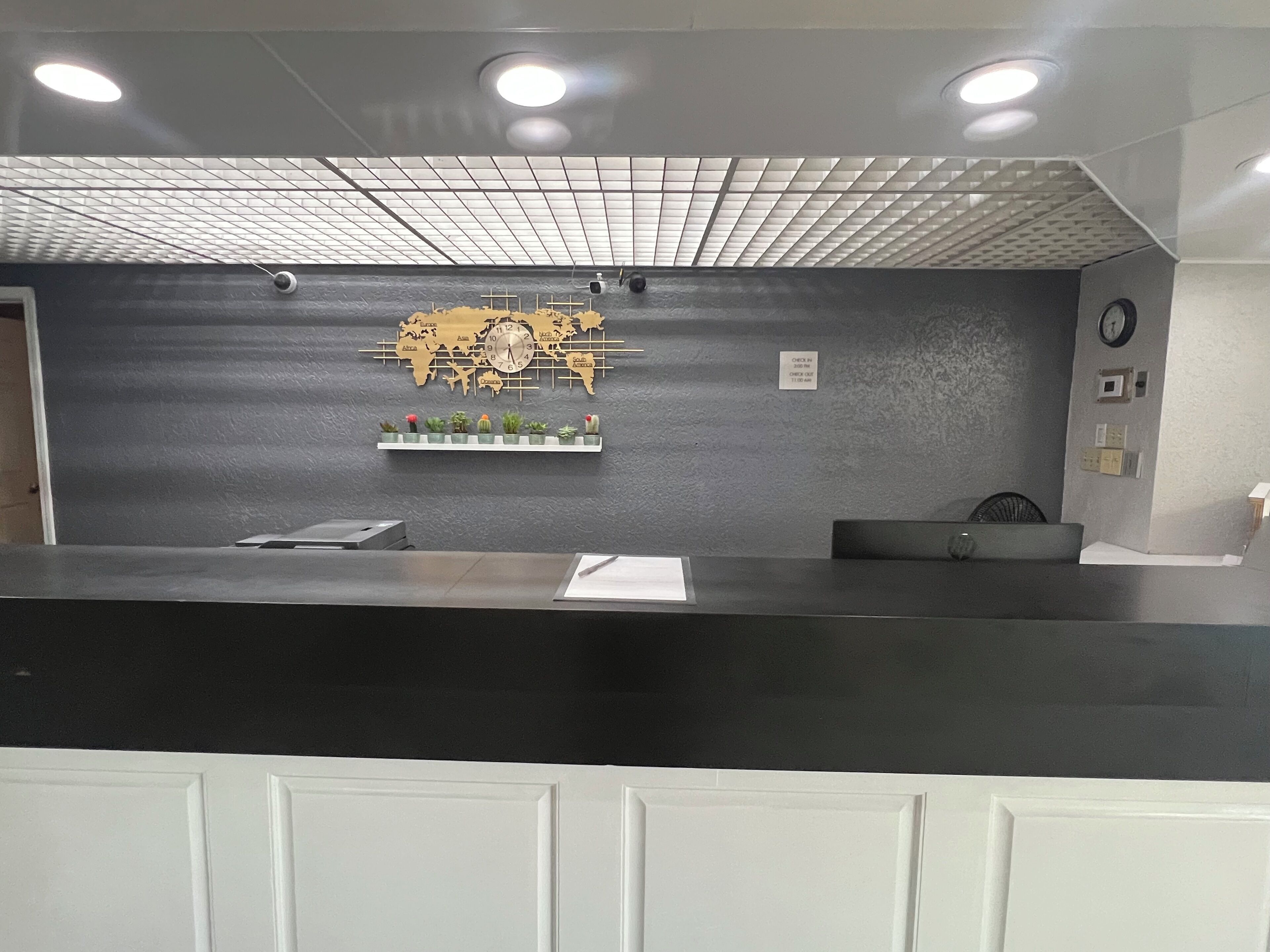 A reception desk with a world map clock, a small plant shelf, and a clock on the wall.