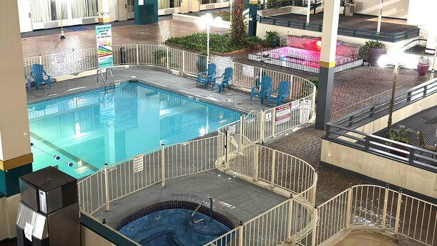 An indoor swimming pool with multiple levels and a hot tub, surrounded by a fenced area with seating.