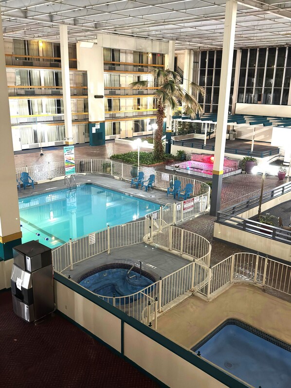 An indoor swimming pool with multiple levels and a hot tub, surrounded by a fenced area with seating.