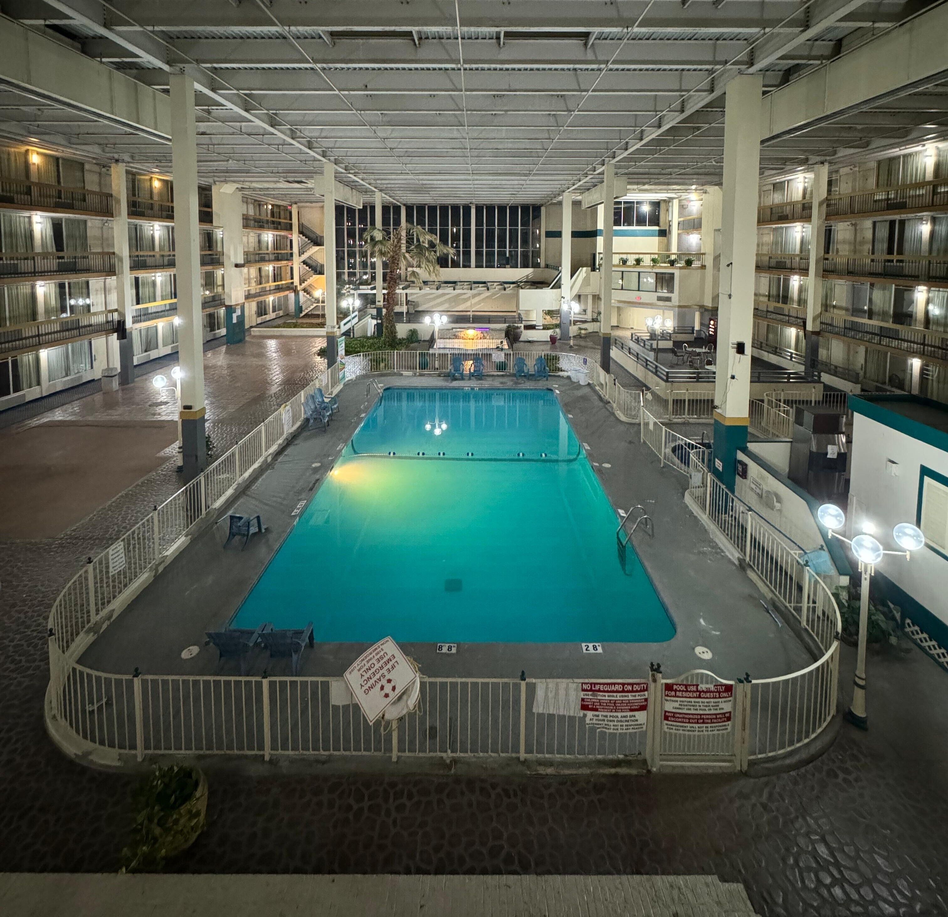 An indoor swimming pool with a tiled deck, surrounded by a white railing and multiple levels of balconies.