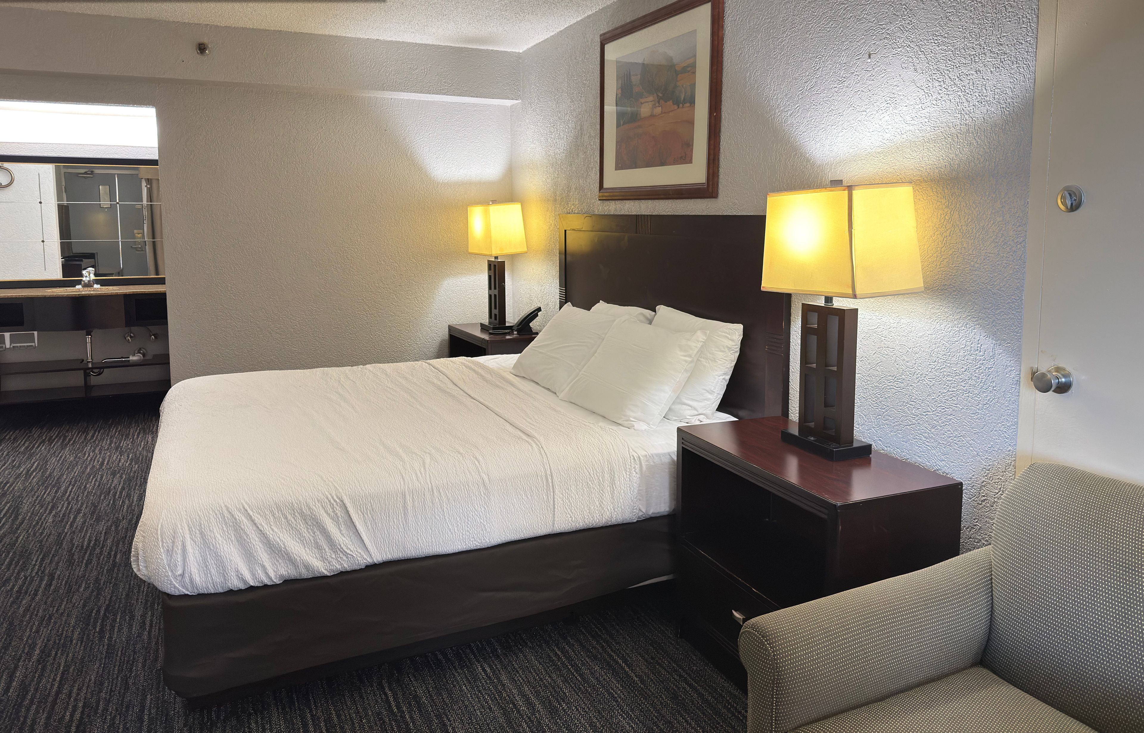 Habitación de hotel en renovación con una cama, dos mesitas de noche con lámparas, un aparador y una silla.