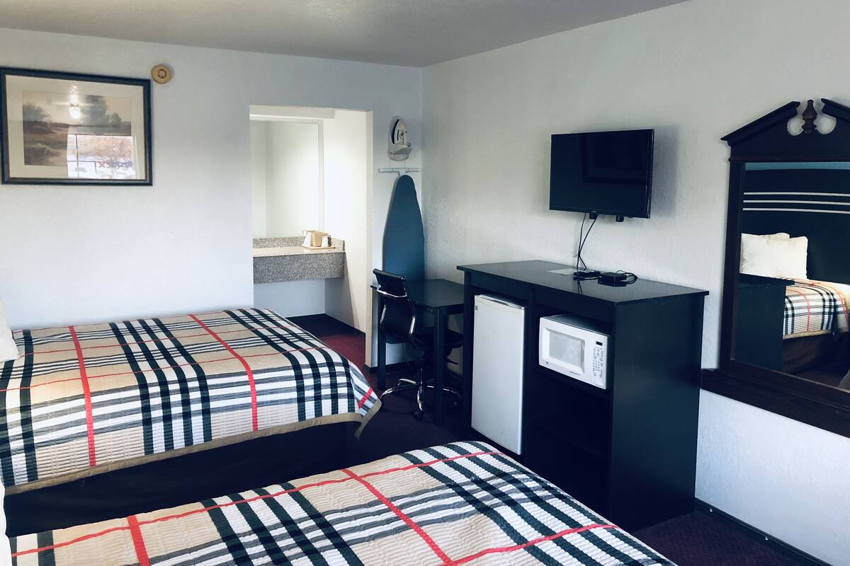 A hotel room with two beds, a desk with a computer, a TV, and a small refrigerator.