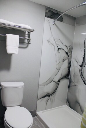 A bathroom with a toilet, a shower with a marble wall, and a towel rack.