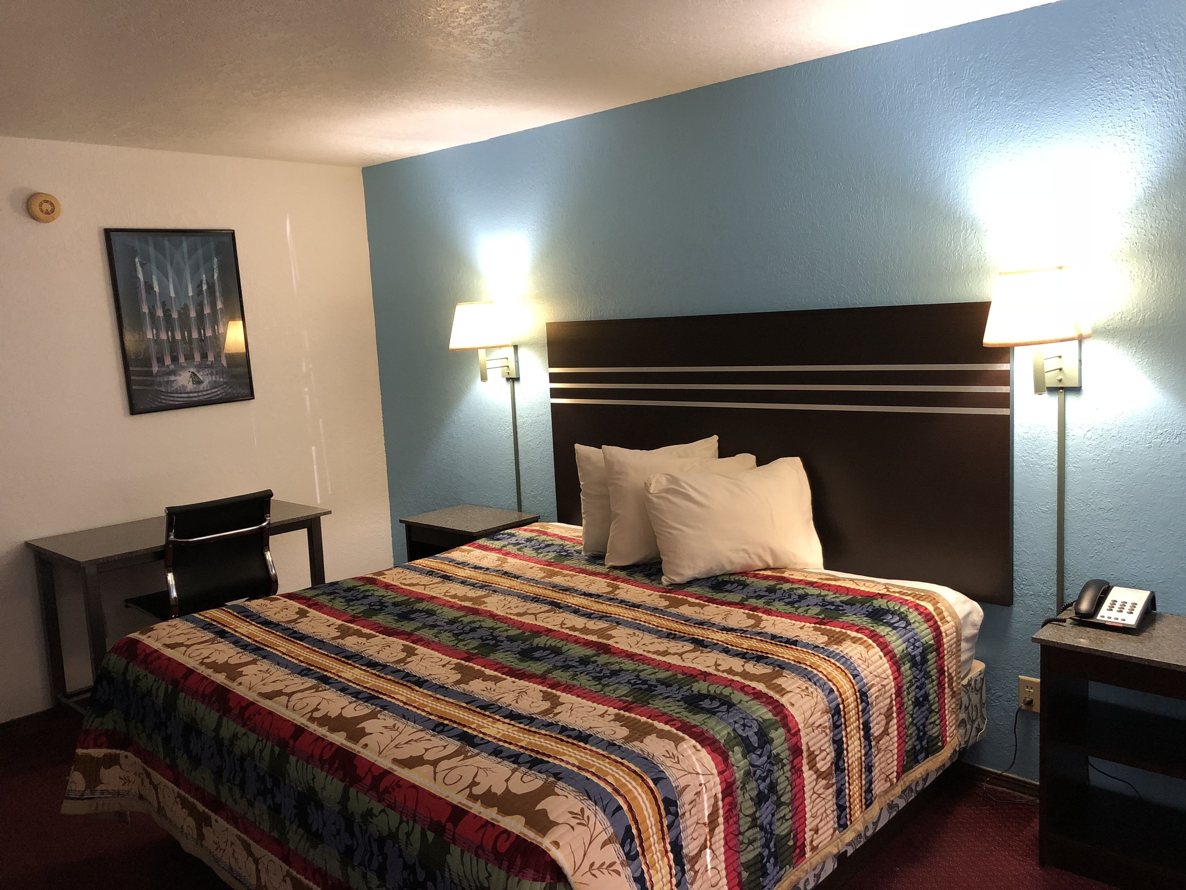 A hotel room with a large bed, two bedside lamps, a desk, and a chair.