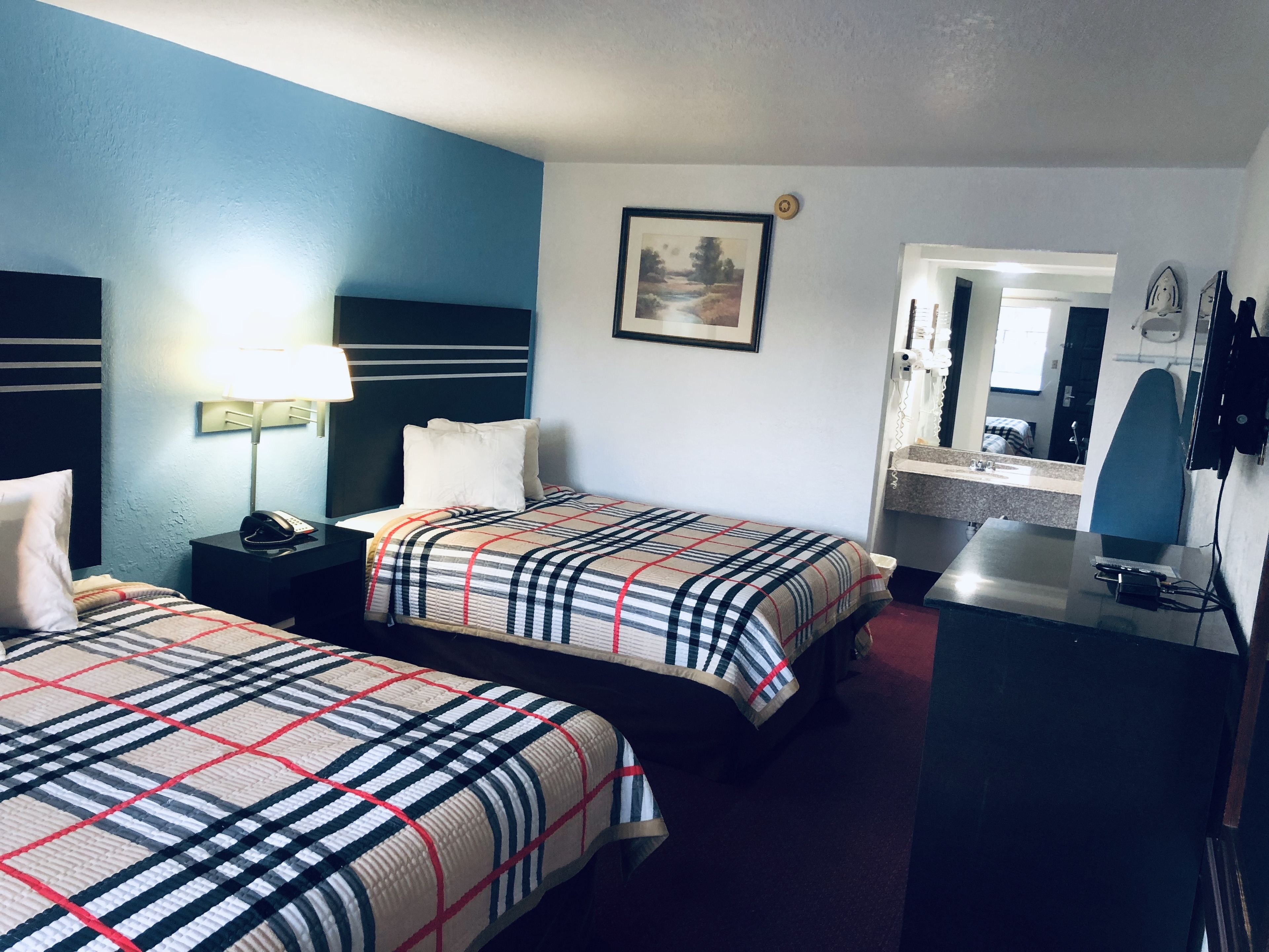 A hotel room with two beds, a desk, a chair, a lamp, a phone, a painting, and a mirror.