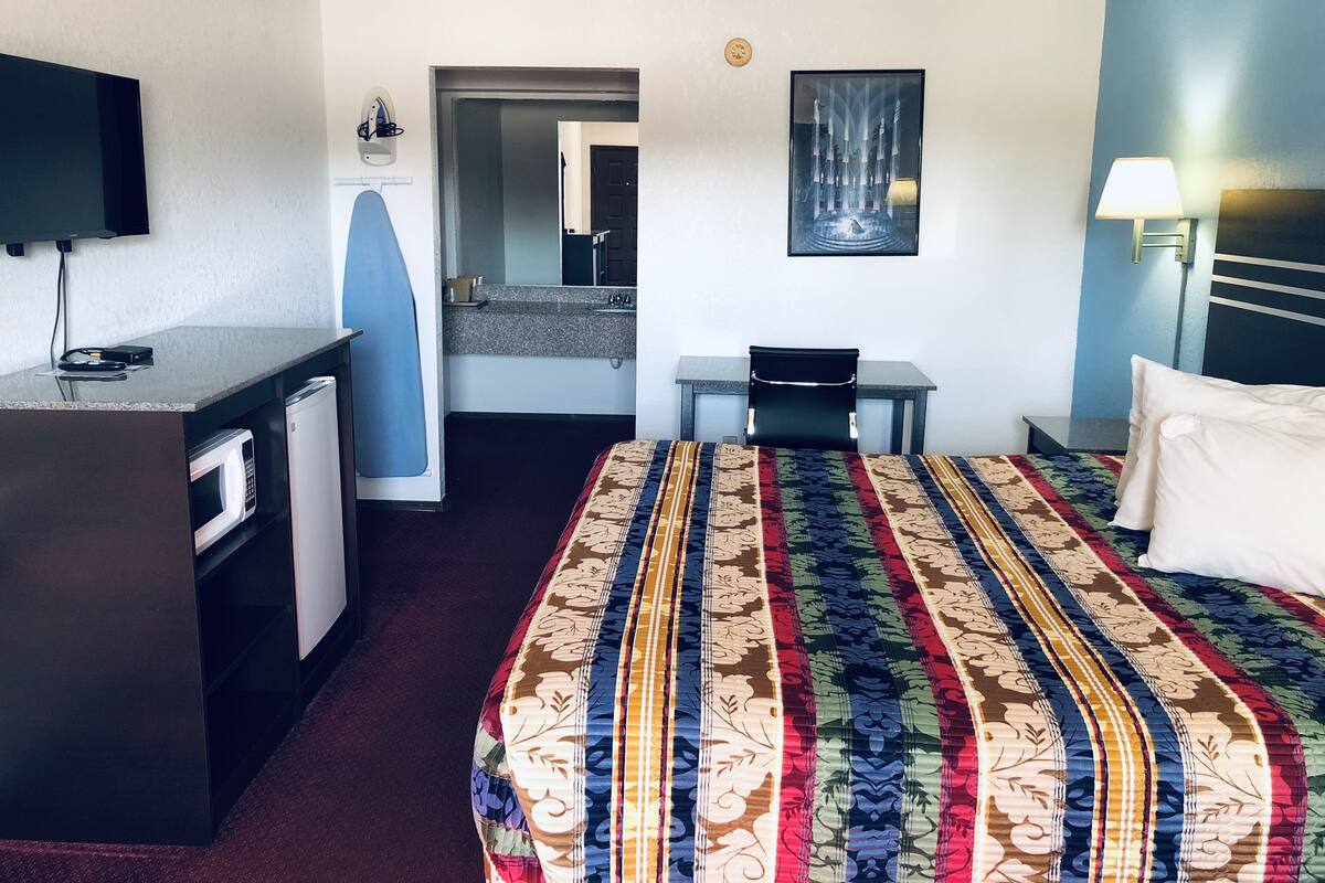 A hotel room with a bed, a desk, a television, a microwave, and a bathroom visible through an open door.