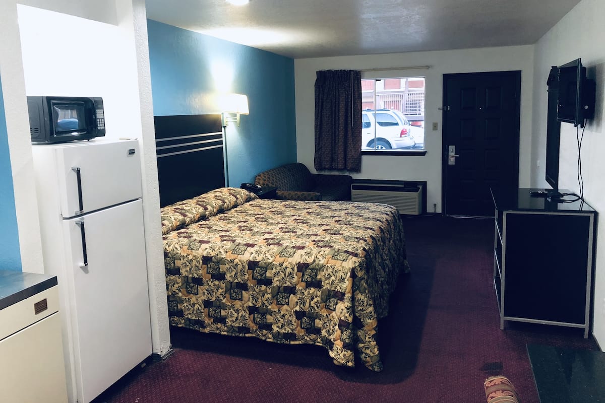 A compact hotel room with a bed, a desk, a TV, a microwave, and a refrigerator.