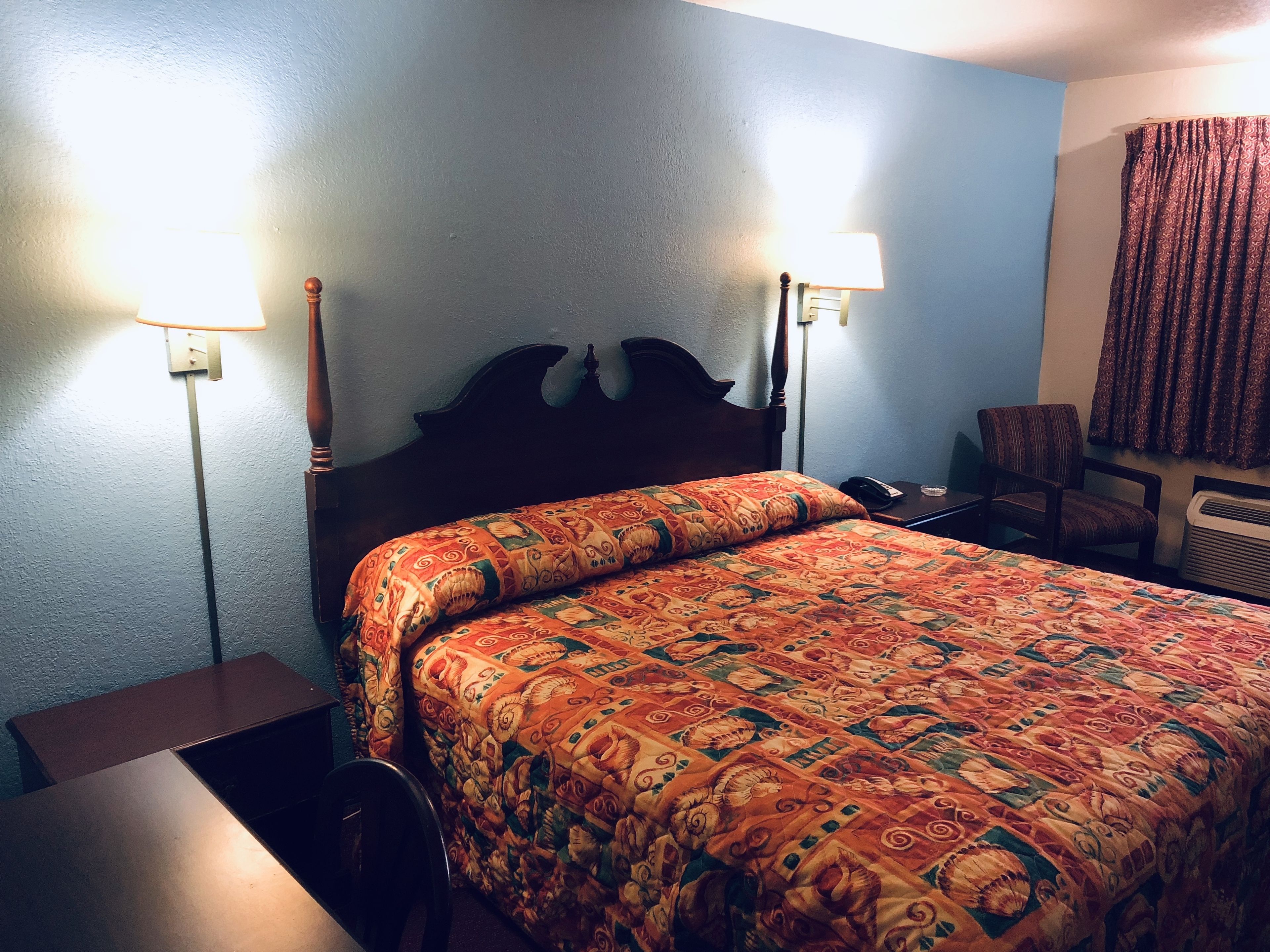 A hotel room with a large bed, two bedside lamps, a chair, a desk, and a window with curtains.