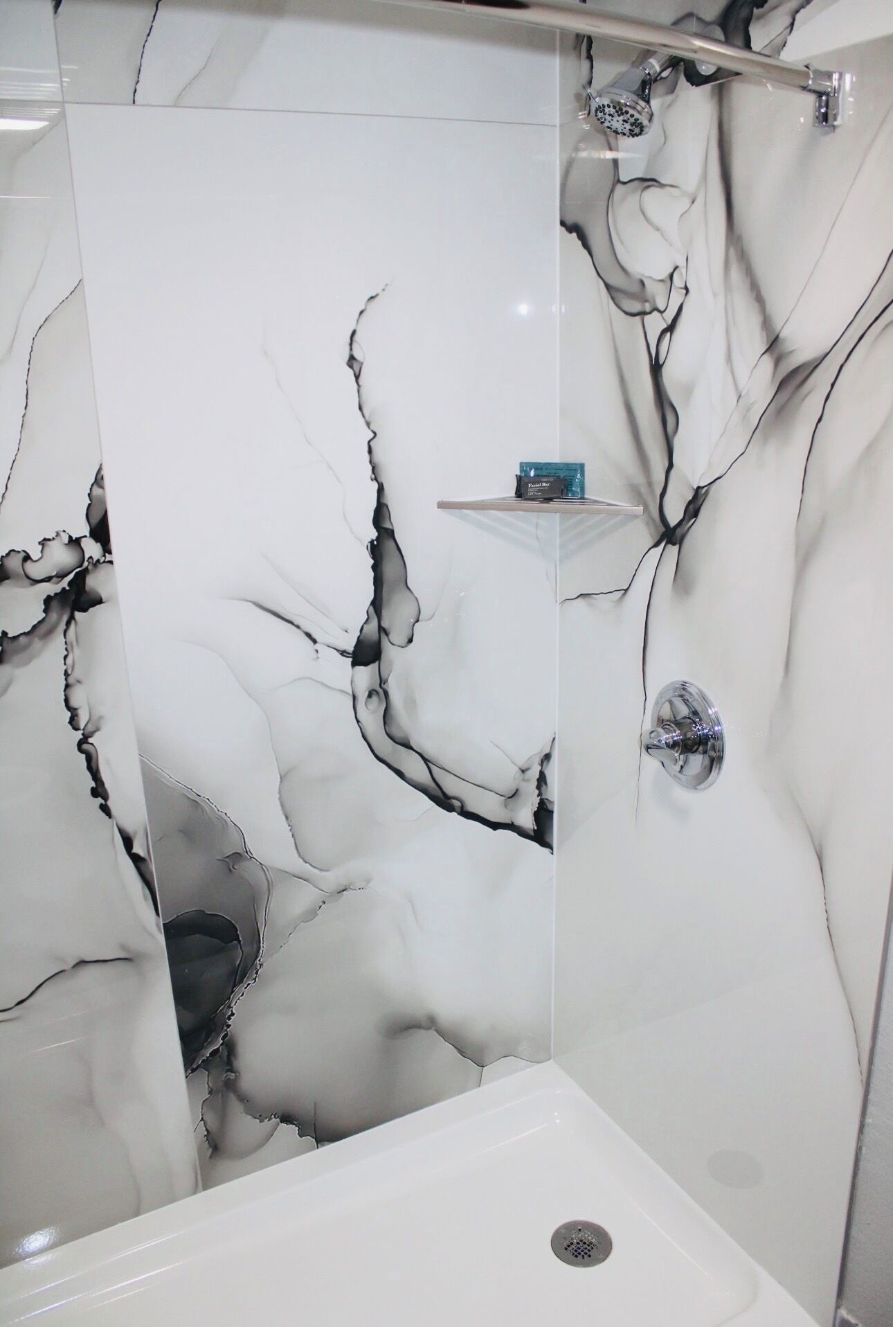 A bathroom with a white marble wall featuring black veins, a shower area, and a small shelf with toiletries.