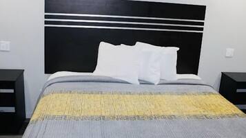 A hotel room with a bed, two bedside tables, a black headboard, and a patterned bedspread.