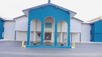 A building with a blue facade, a central entrance with three arches, and a parking lot in front.