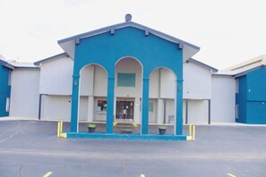 A building with a blue facade, a central entrance with three arches, and a parking lot in front.