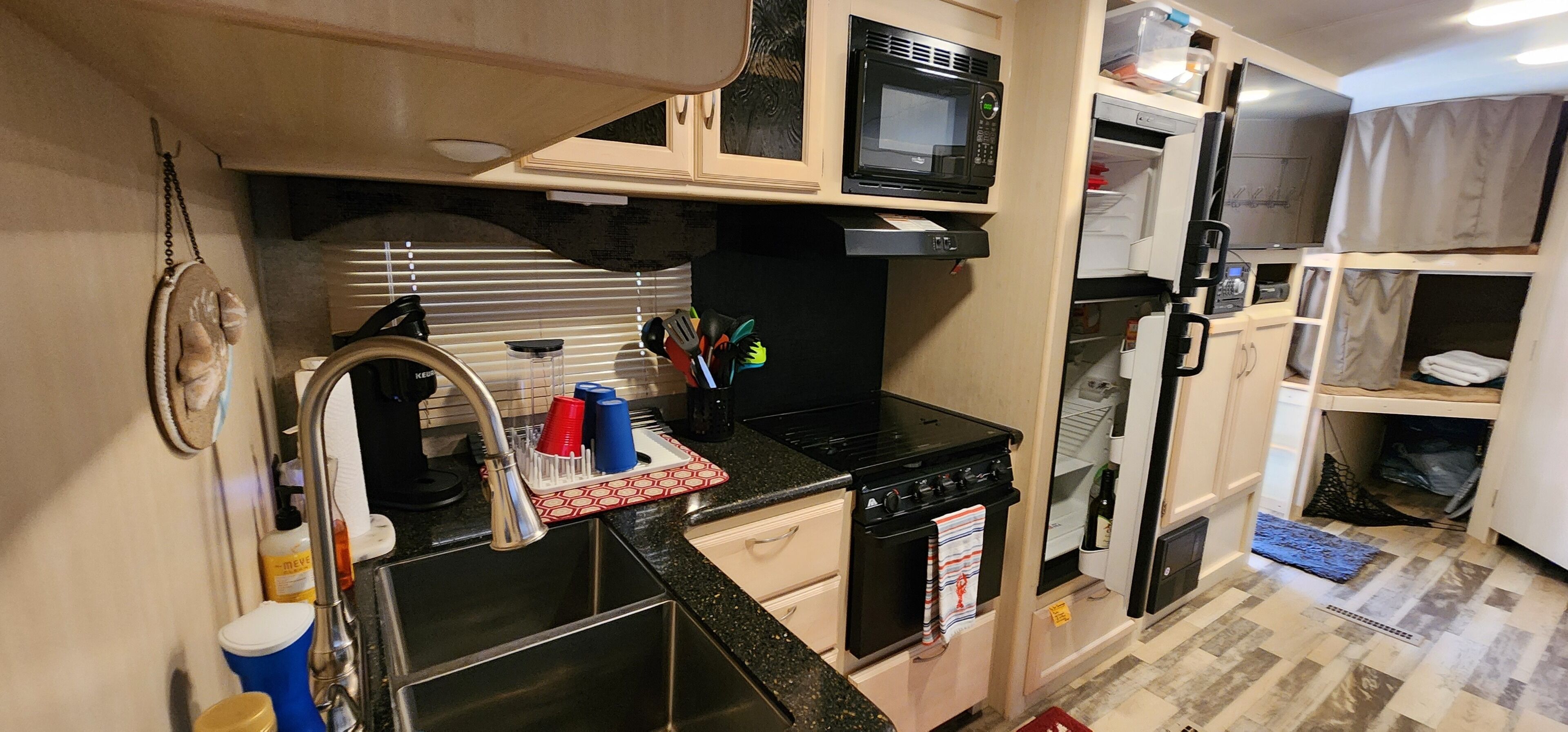 A compact kitchenette with a microwave, stove, sink, and storage cabinets.
