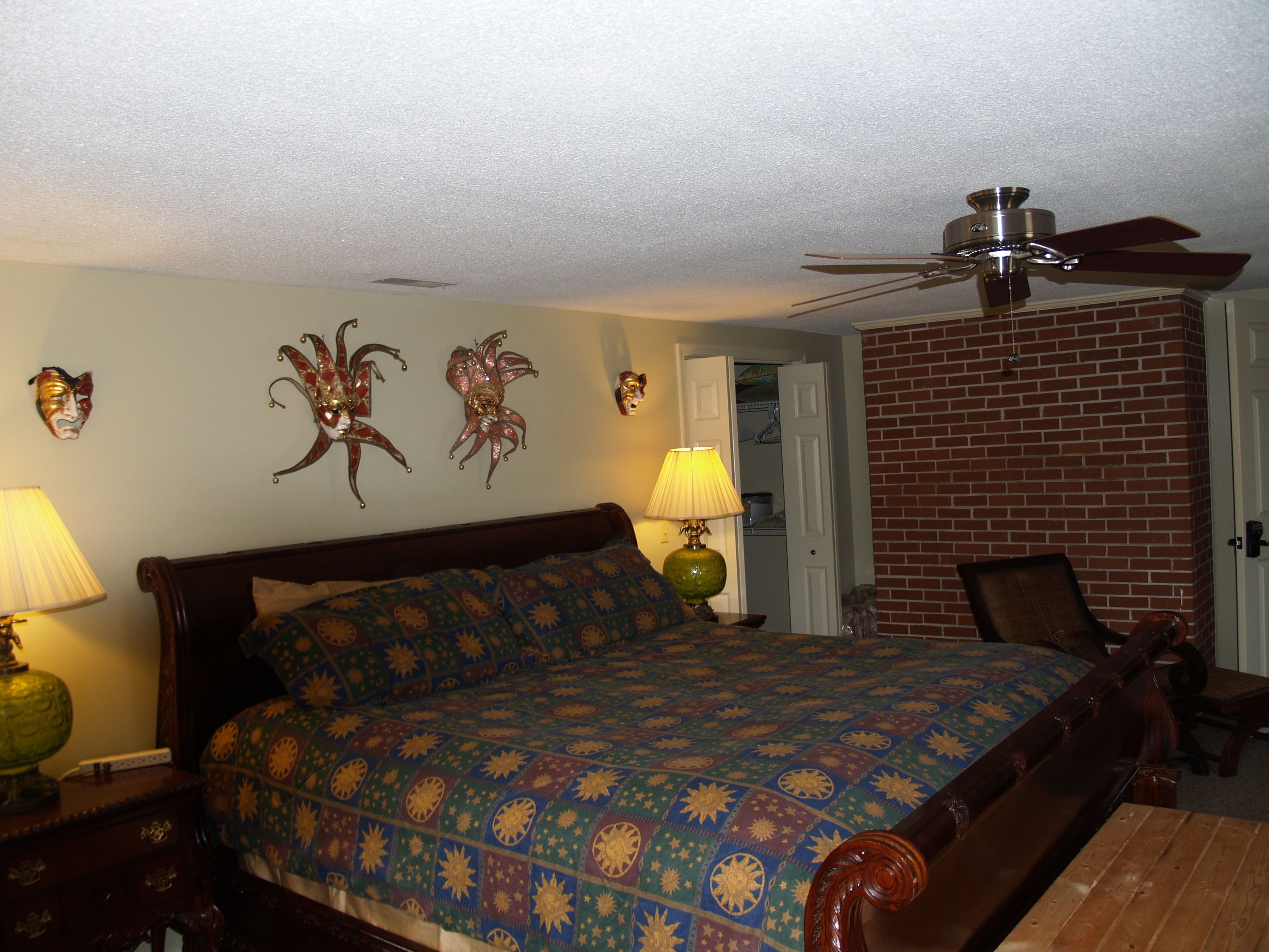 A bedroom with a bed, a ceiling fan, two wall-mounted lamps, and a brick wall.