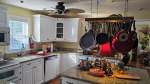 Une cuisine avec des armoires blanches, une cuisinière, un four à micro-ondes et un ventilateur de plafond.